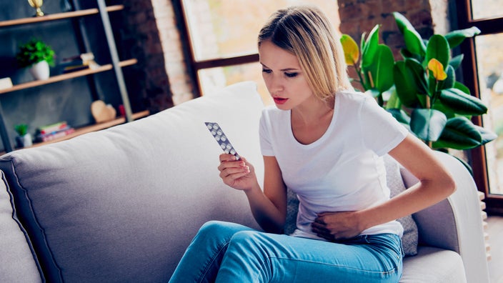 A person with a stomachache looking at a blister pack.