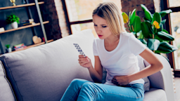 A person with a stomachache looking at a blister pack.
Deagreez/iStock via Getty Images Plus 