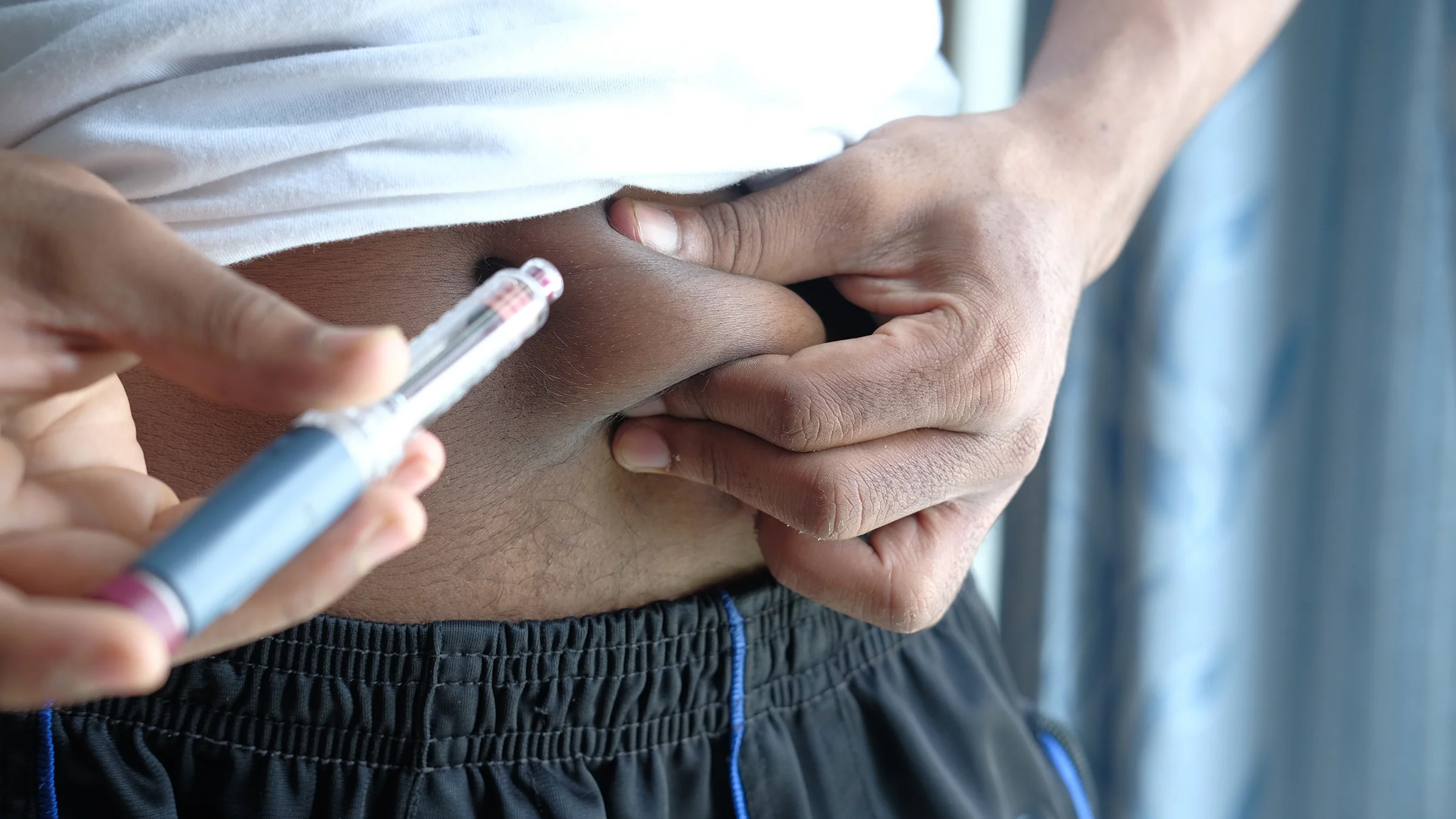 Close-up of a man using his injection pen. He is pinching his stomach at the injection site.