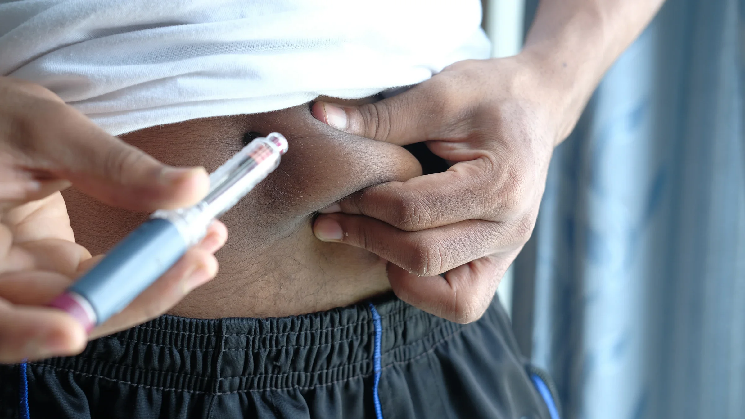 Close-up of a man using his injection pen. He is pinching his stomach at the injection site.
towfiqu ahamed/iStock via Getty Images
