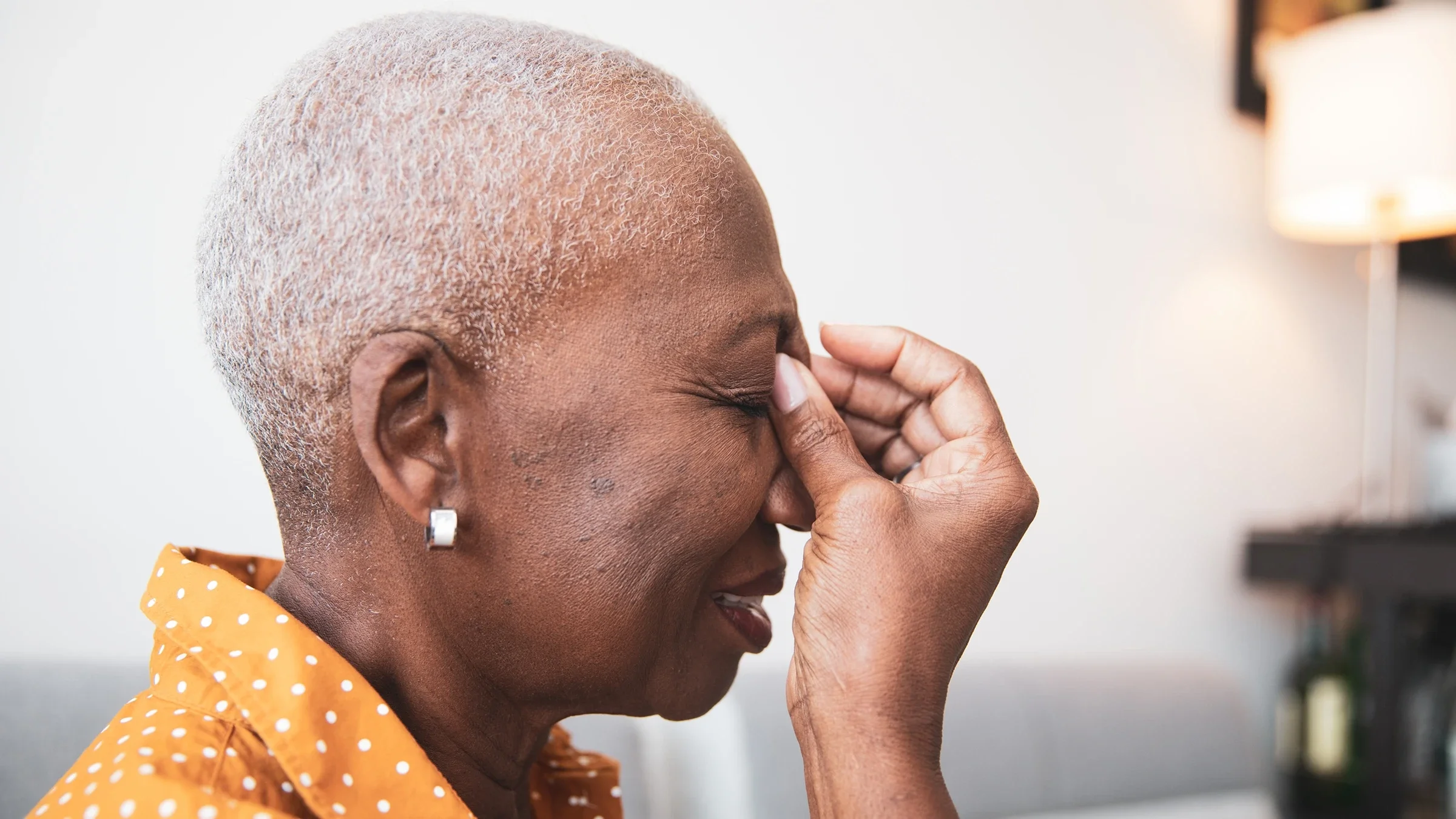Side-profile portrait of a woman with sinus pain. She is pinching the bridge of her nose and squinting in pain.