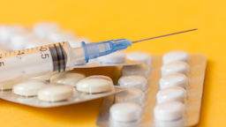 Needle and pill packs on a yellow background.
golibtolibov/iStock via Getty Images
