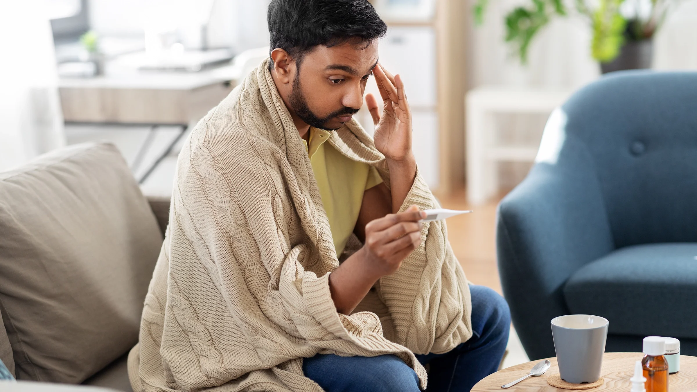 A person wrapped in a blanket checks a thermometer.