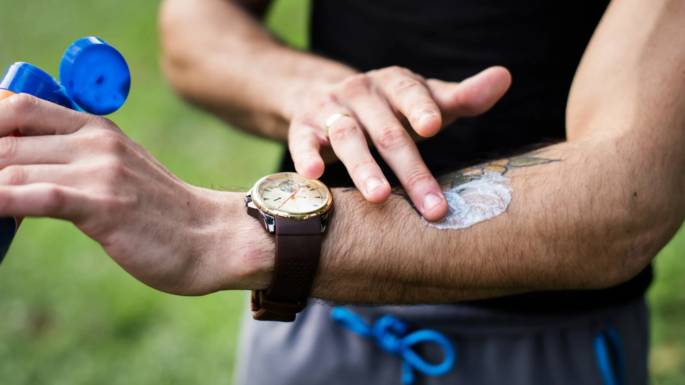 Close-up of a person applying sunscreen to a tattoo on their arm.
