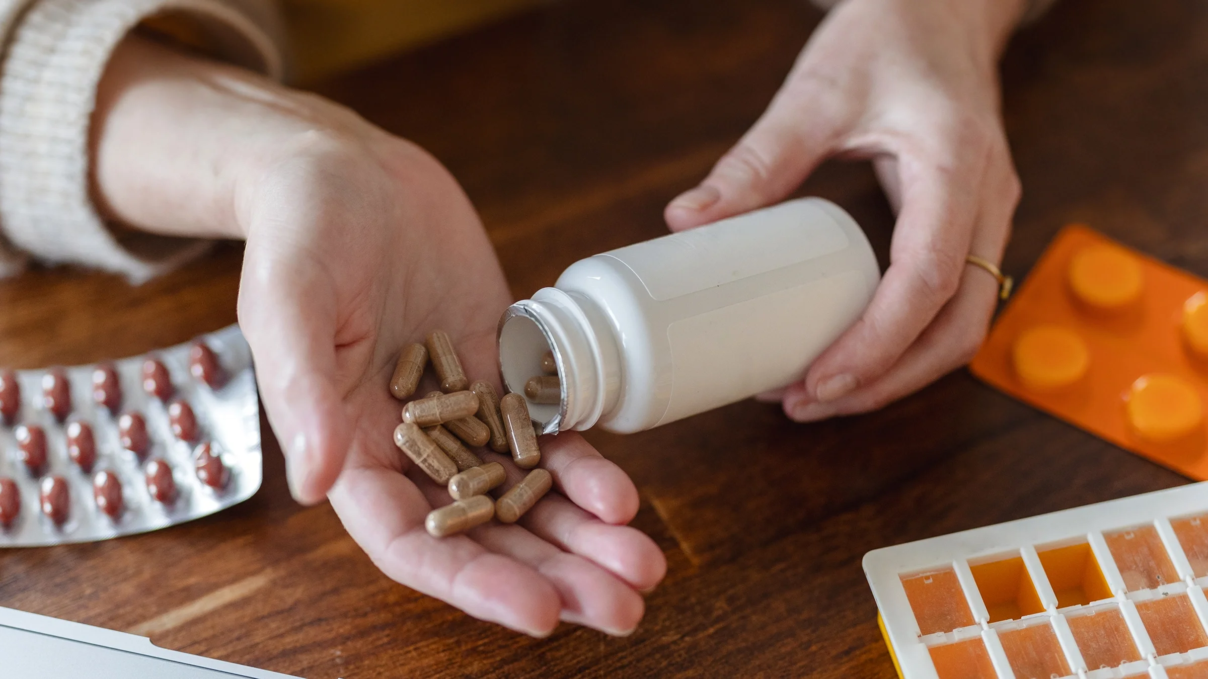 A woman pours supplement pills from a bottle onto the palm of her hand. 