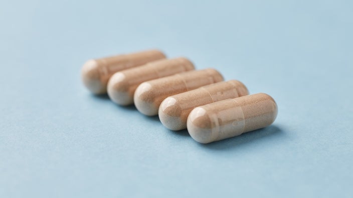 Five tan supplement capsules set on a diagonal direction on a light blue background.