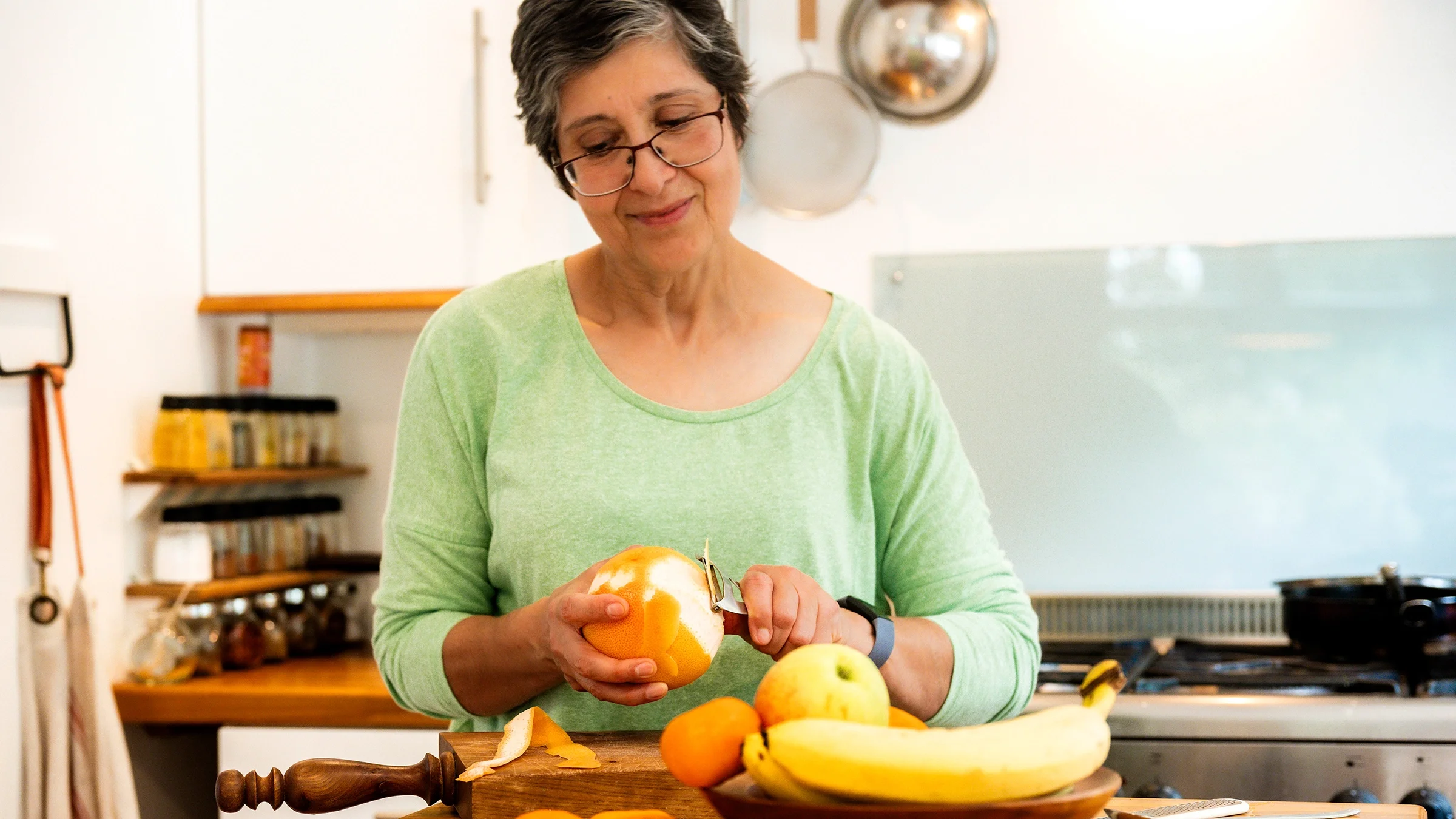 A woman peels a grapefruit in her kitchen.
