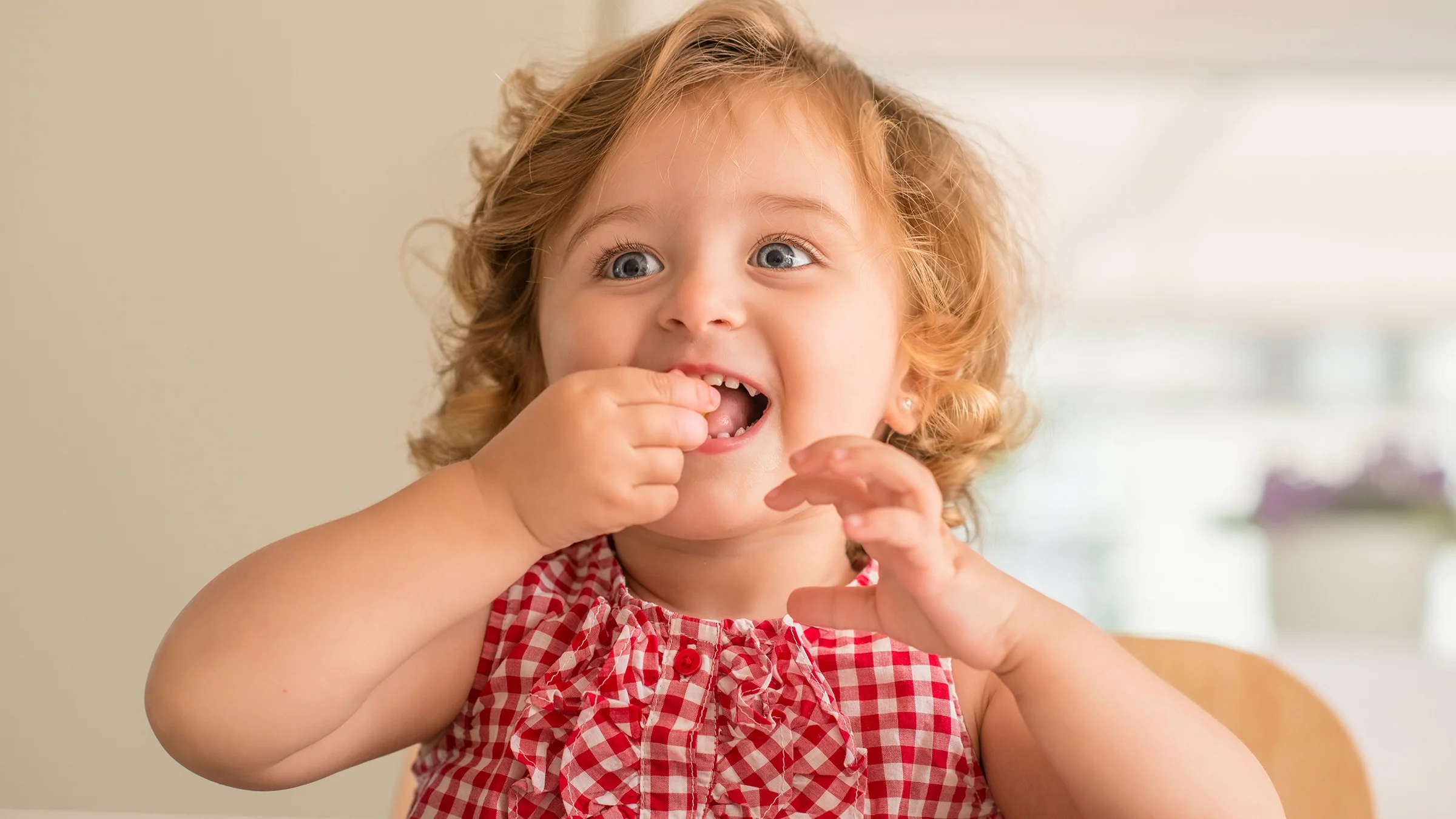 Portrait of a cute curly haired toddler putting something in their mouth to eat.