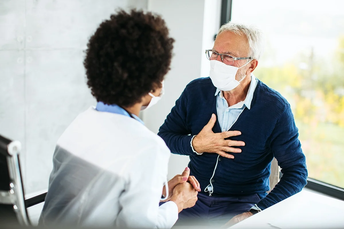Elderly patient explaining chest pain to his doctor at a visit. It is an over the should perspective looking at the patient with doctor's back towards the camera.