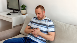 Man sitting on couch with stomach pain.
Jelena Stanojkovic/iStock via Getty Images