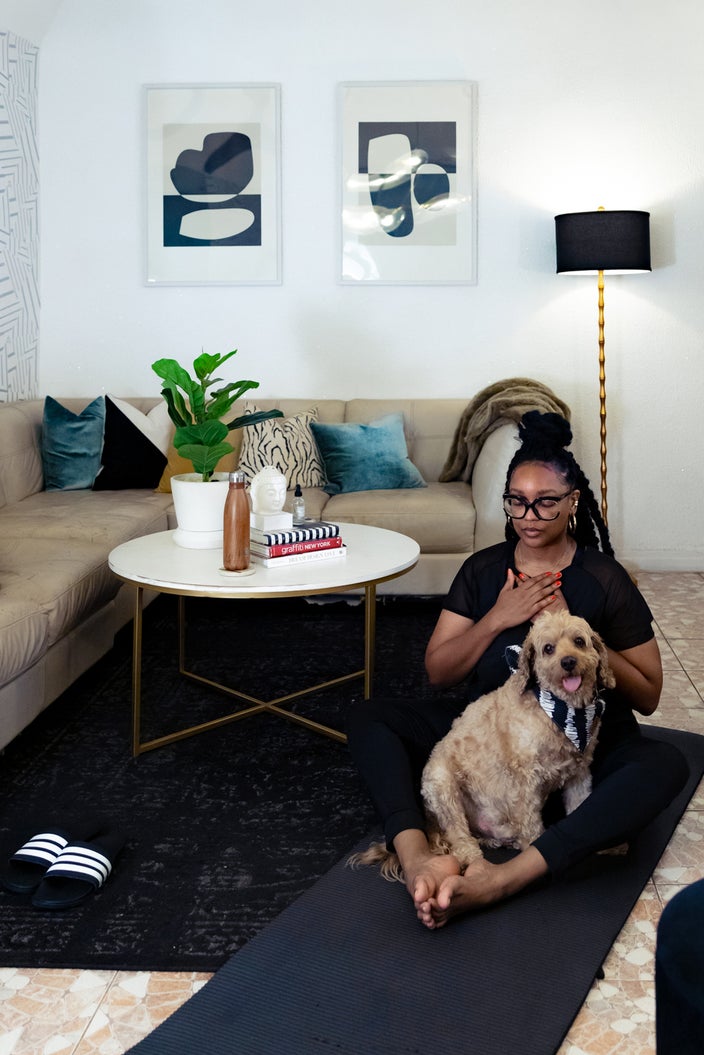 Nikki Nurse at home practicing yoga and meditation in her living room. Her dog is sitting with her on her yoga mat. 