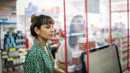Two young women standing at the pharmacy counter looking through the plexiglass screen.
FG Trade/E+ via Getty Images
