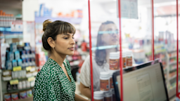Two young women standing at the pharmacy counter looking through the plexiglass screen.
FG Trade/E+ via Getty Images
