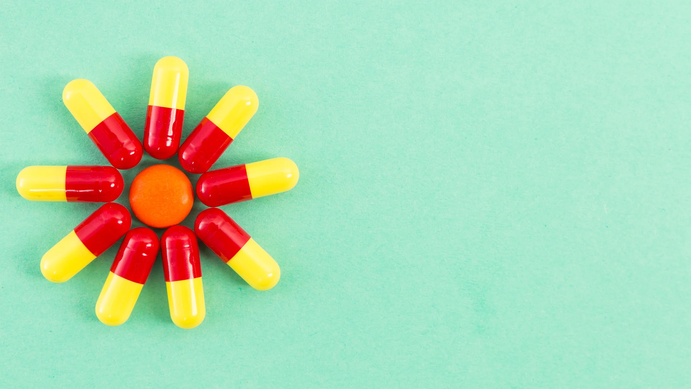 Sunburst pattern made out of yellow and red pills on a green background.