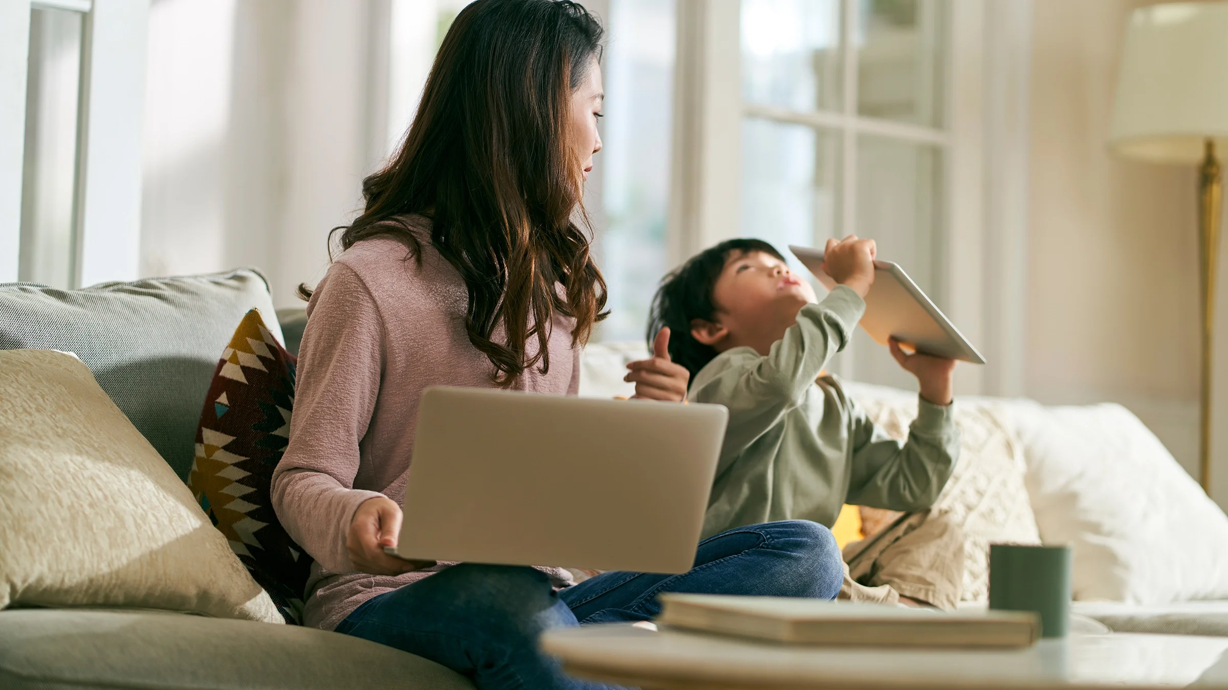 A mother with a laptop sits next to her son on the sofa. ADHD is underdiagnosed in the Asian American community. 