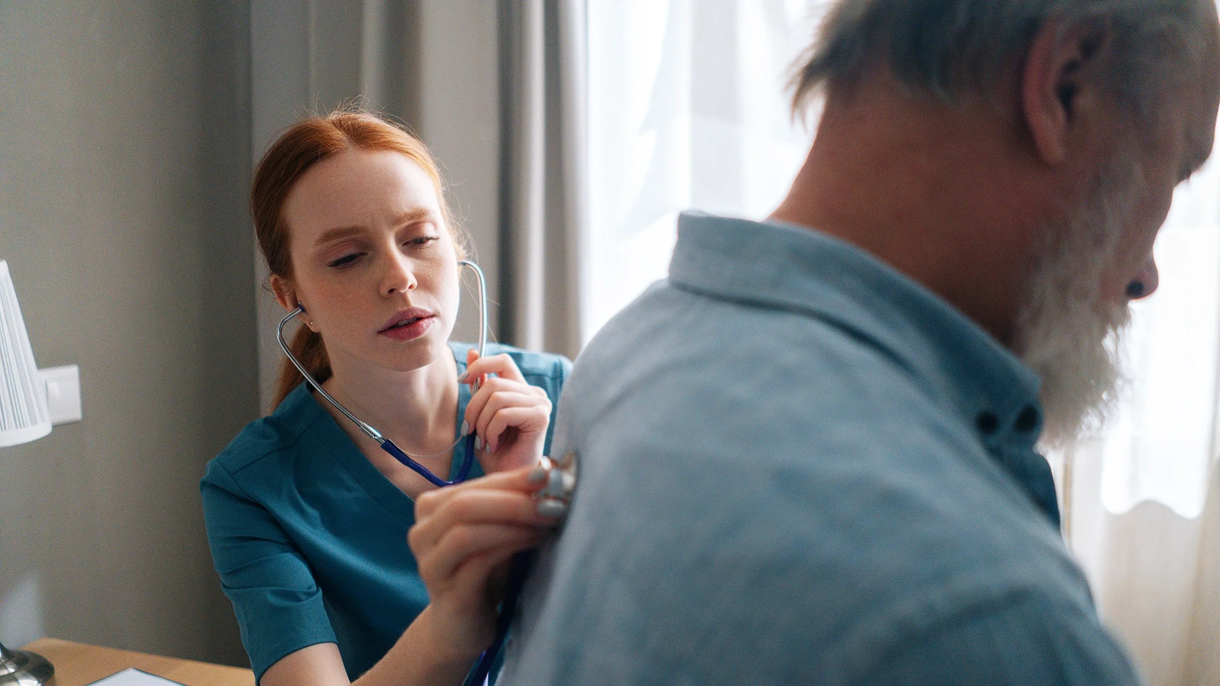 Close-up of doctor examining lungs of older patient at home using stethoscope