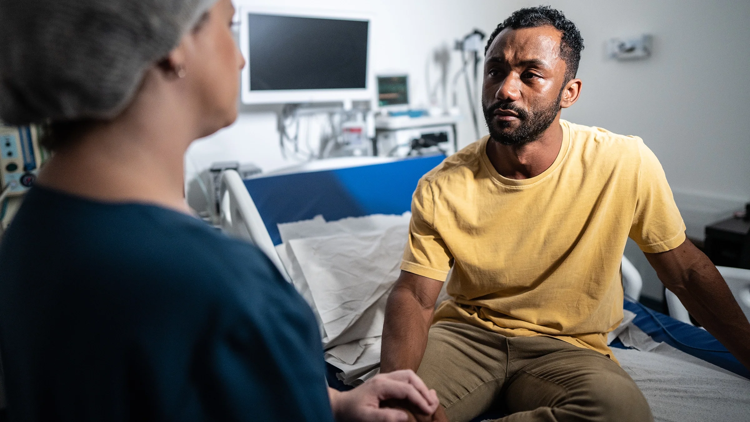 A person is listening to a medical professional while sitting on a hospital bed.