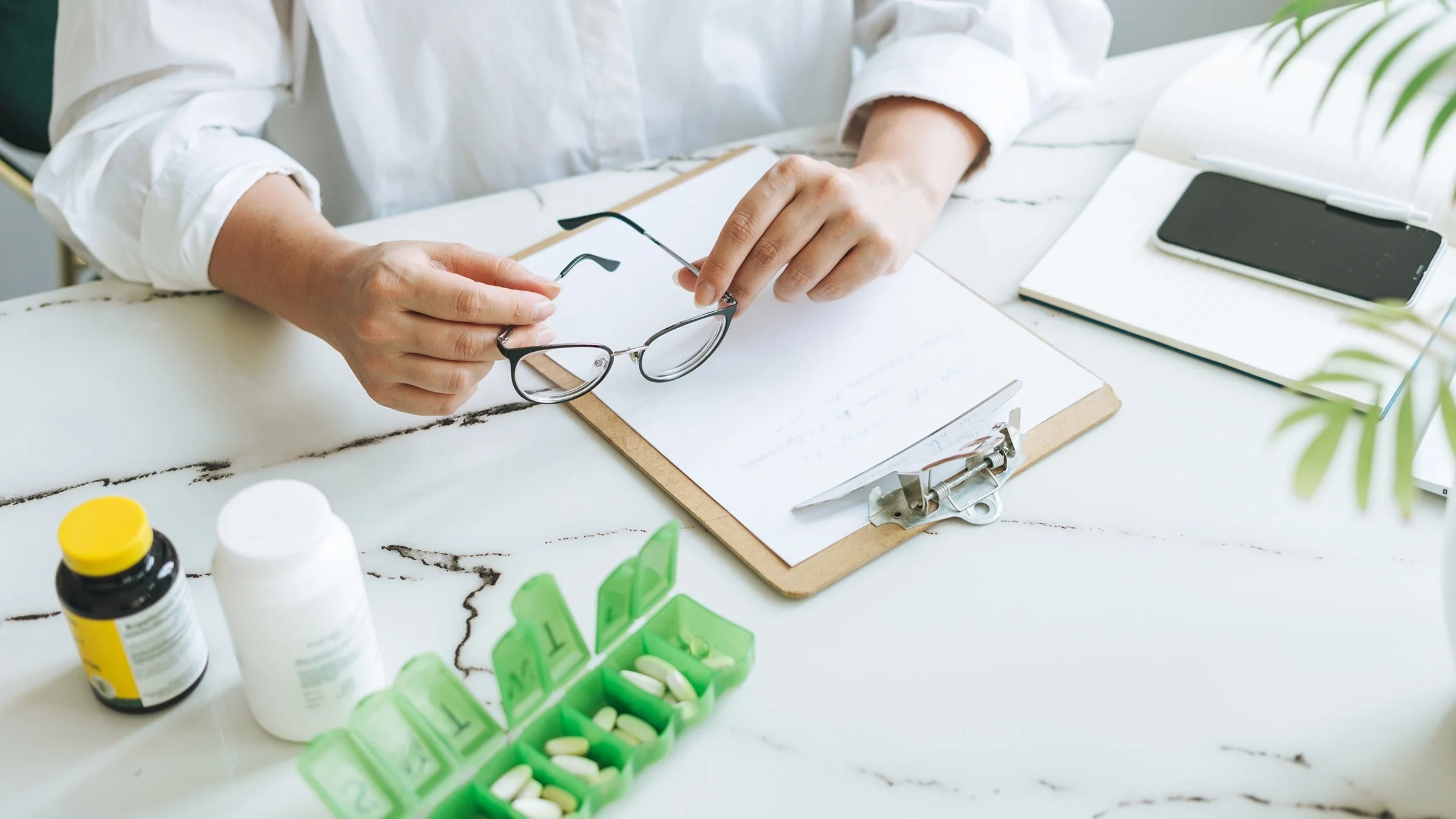 Cropped shot of a person creating a list of their medications. They have supplement bottles and a green pill organizer next to them.