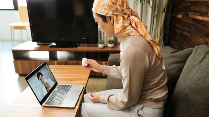 A cancer patient in a telehealth call holding a pill bottle.