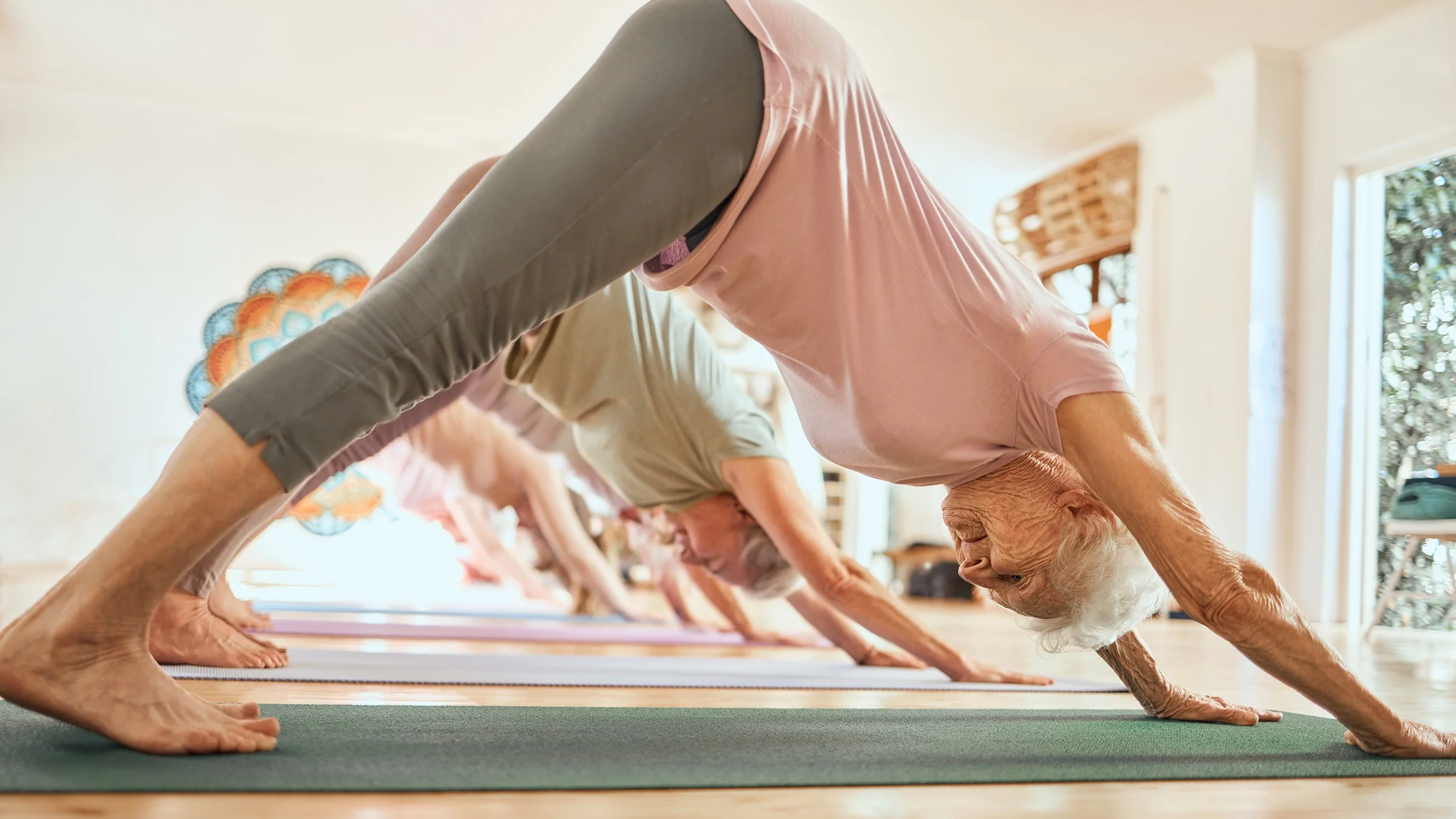 A senior woman is shown doing the downward dog pose in yoga class.