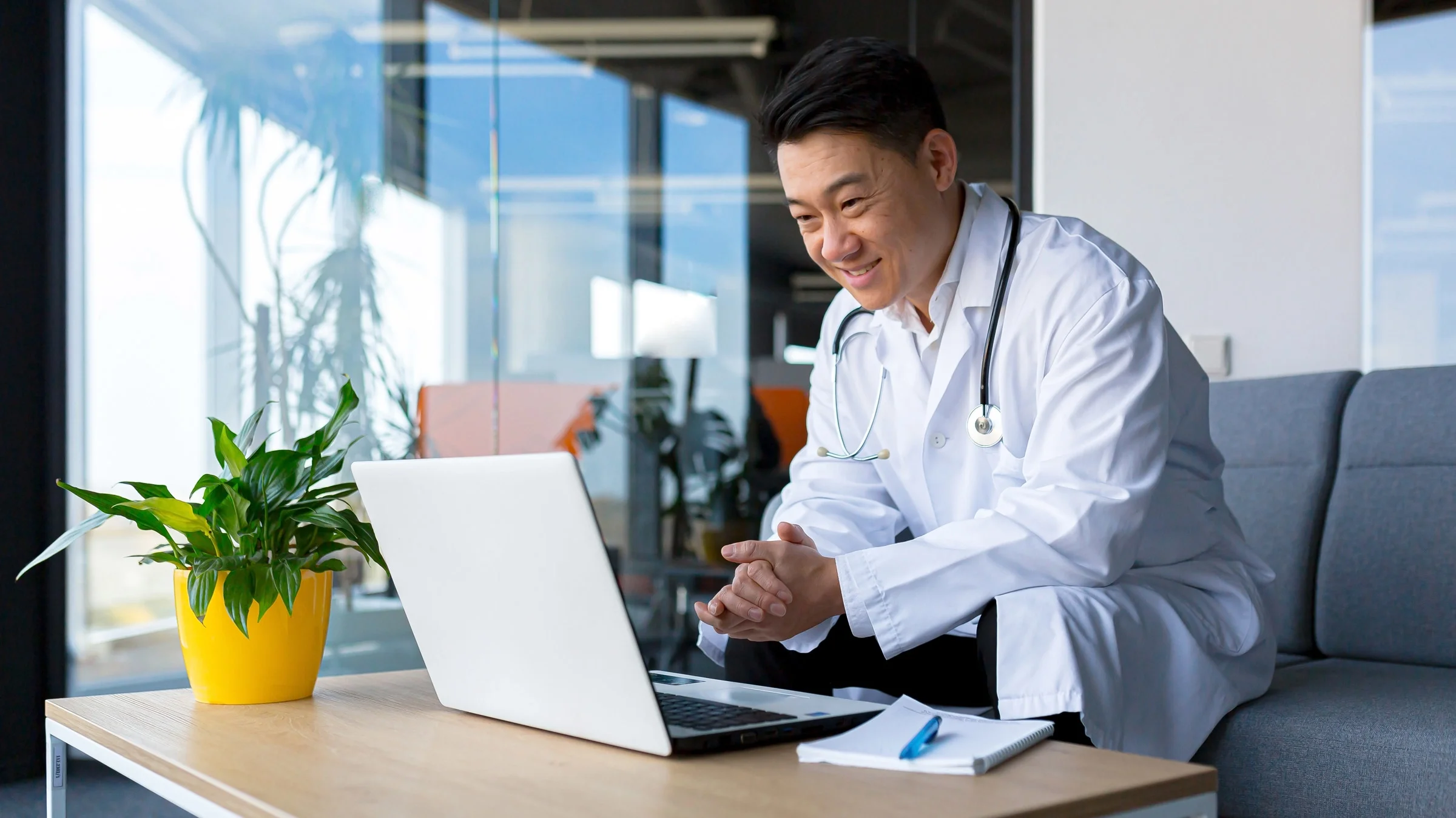 A doctor talking to a patient via telehealth on a couch in an office.