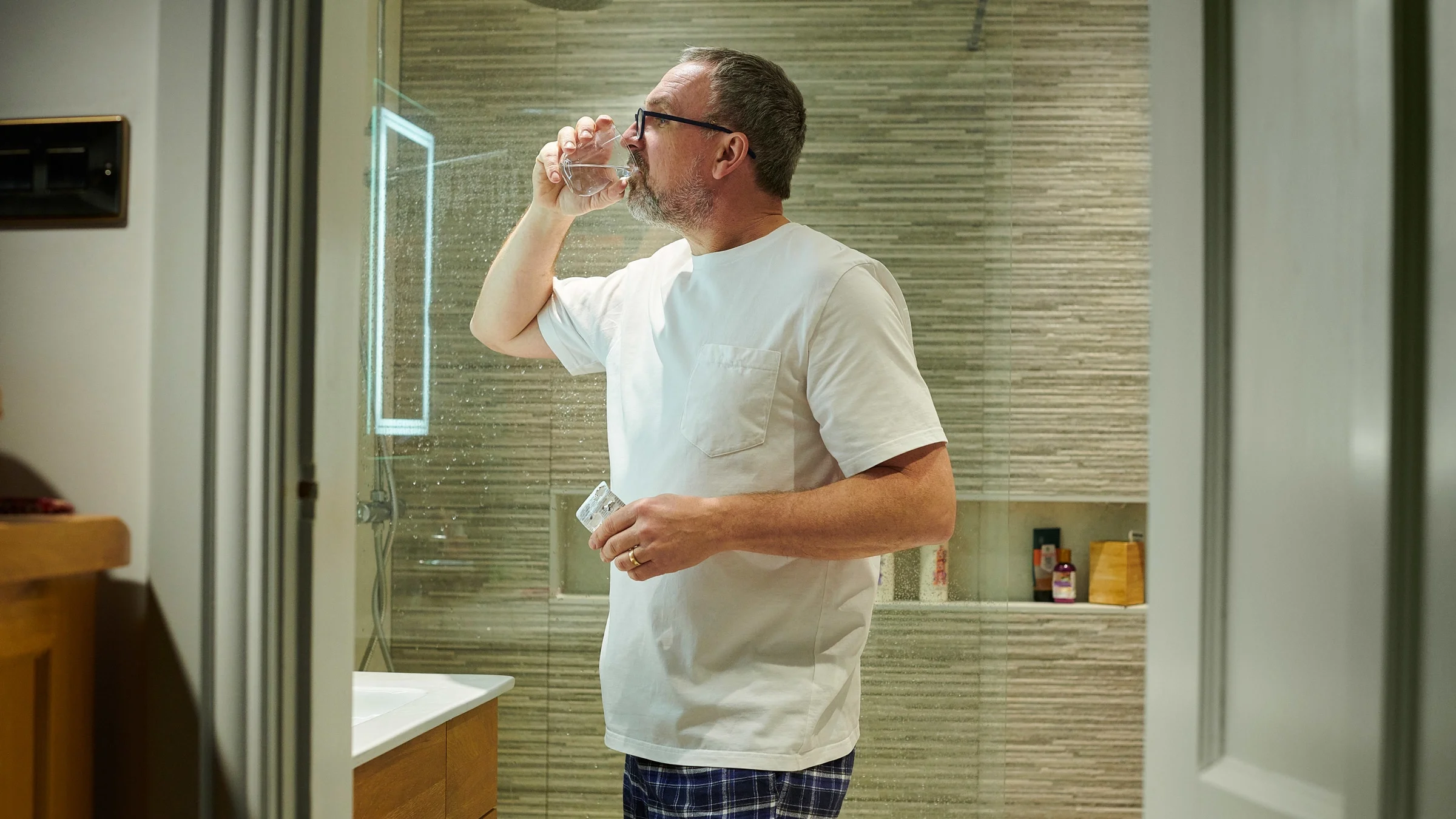 A man taking a pill in his bathroom before bedtime.