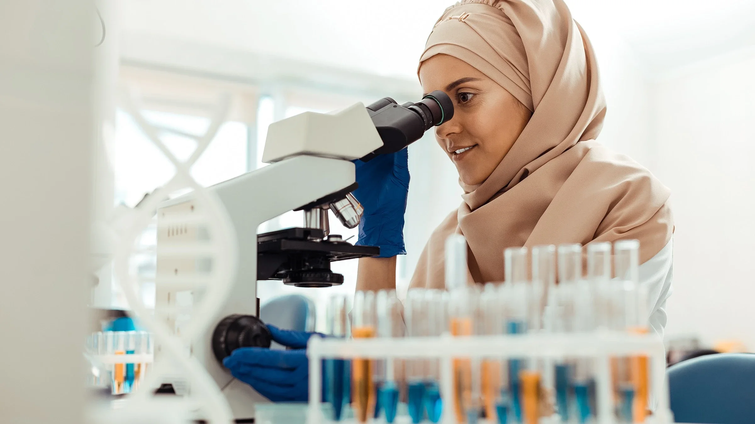 Young woman wearing head scarf working in a lab looking into a microscope