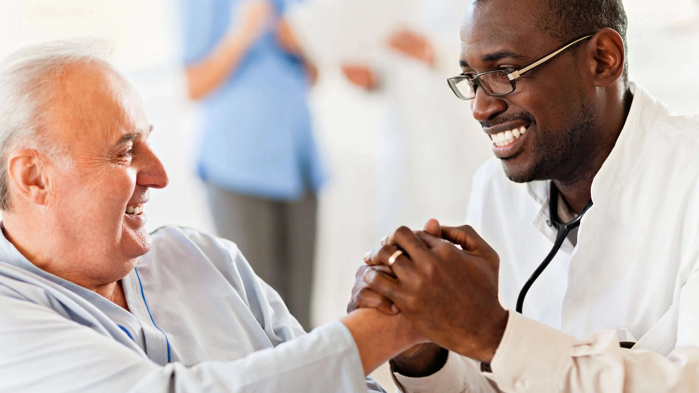 Senior man shaking his doctor’s hand. The doctor is using both hands to hold the patient's hand.