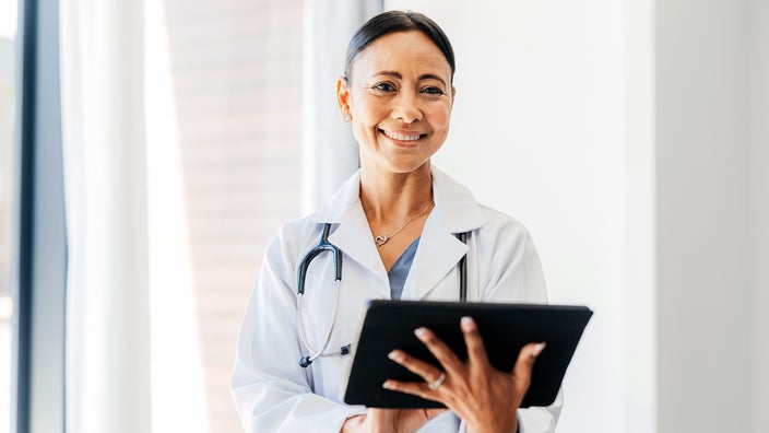 Portrait of a doctor smiling while holding a tablet.