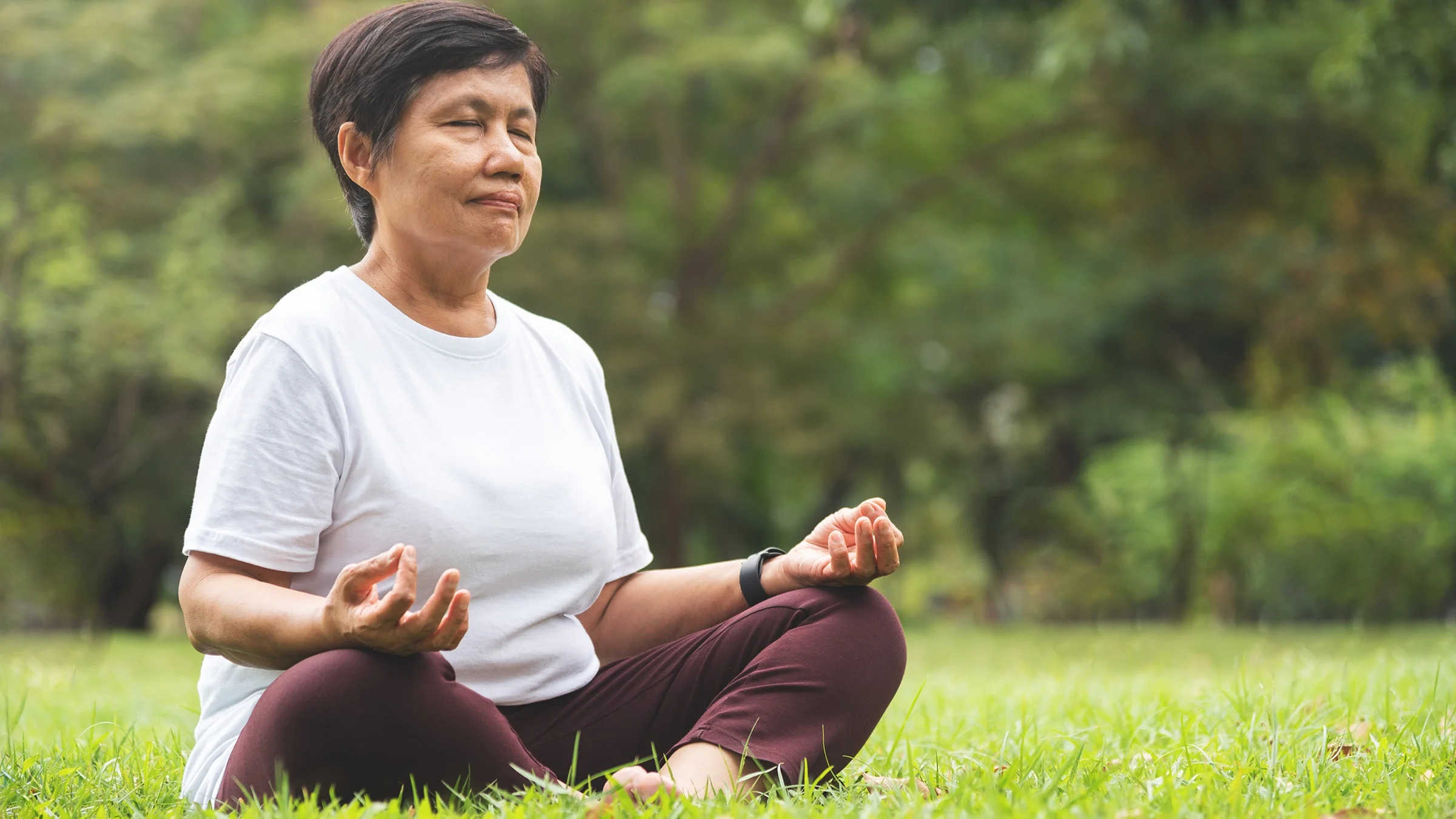 An older woman is meditating in the park.