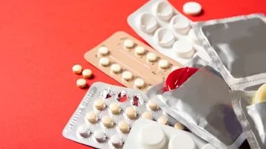 Birth control pills and condoms on a red background.
Inna Mykhalchuk/iStock via Getty Images Plus 