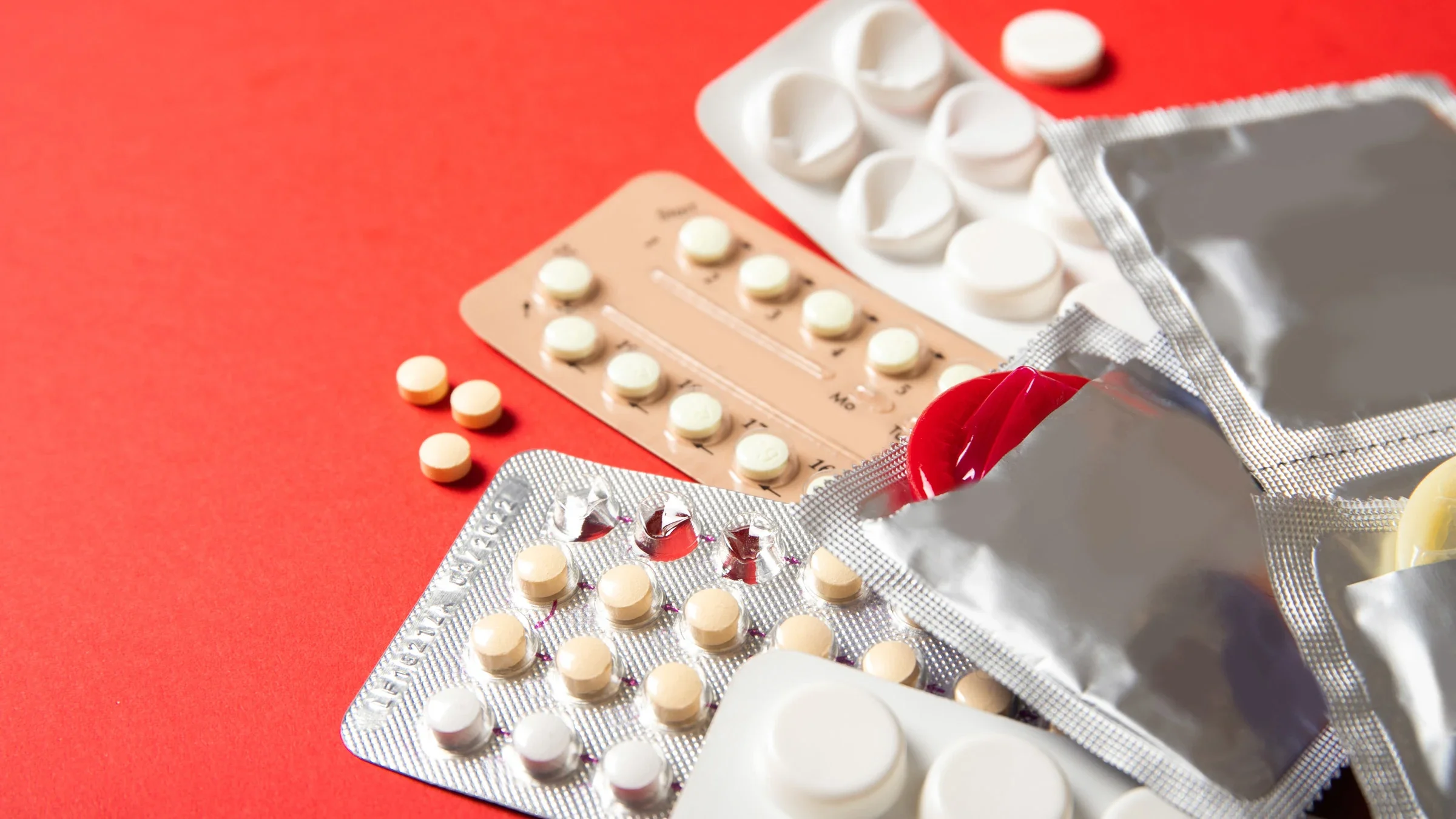 Birth control pills and condoms on a red background.
Inna Mykhalchuk/iStock via Getty Images Plus 