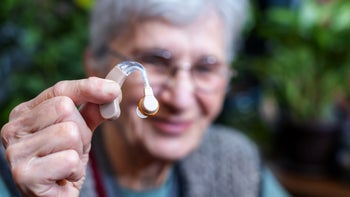 Health: Ear health: senior woman holding hearing aid up-1317347073