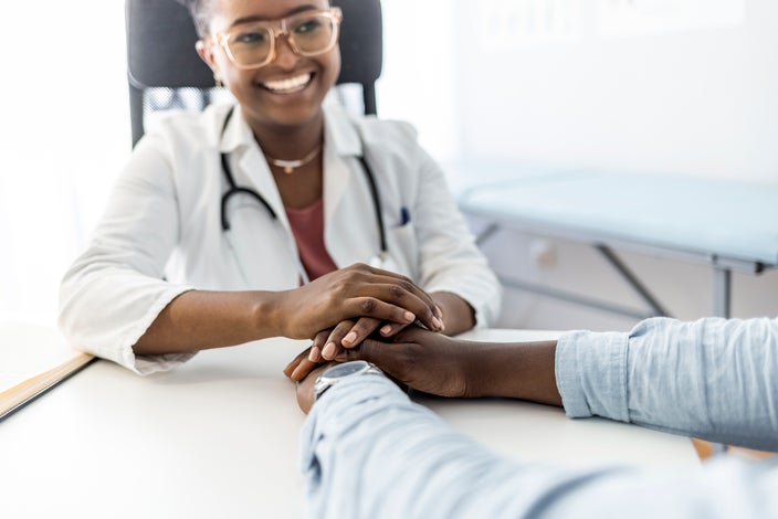 Smiling doctor holding a patient's hands across the table. The patient isn't visible, just their hands and arms.