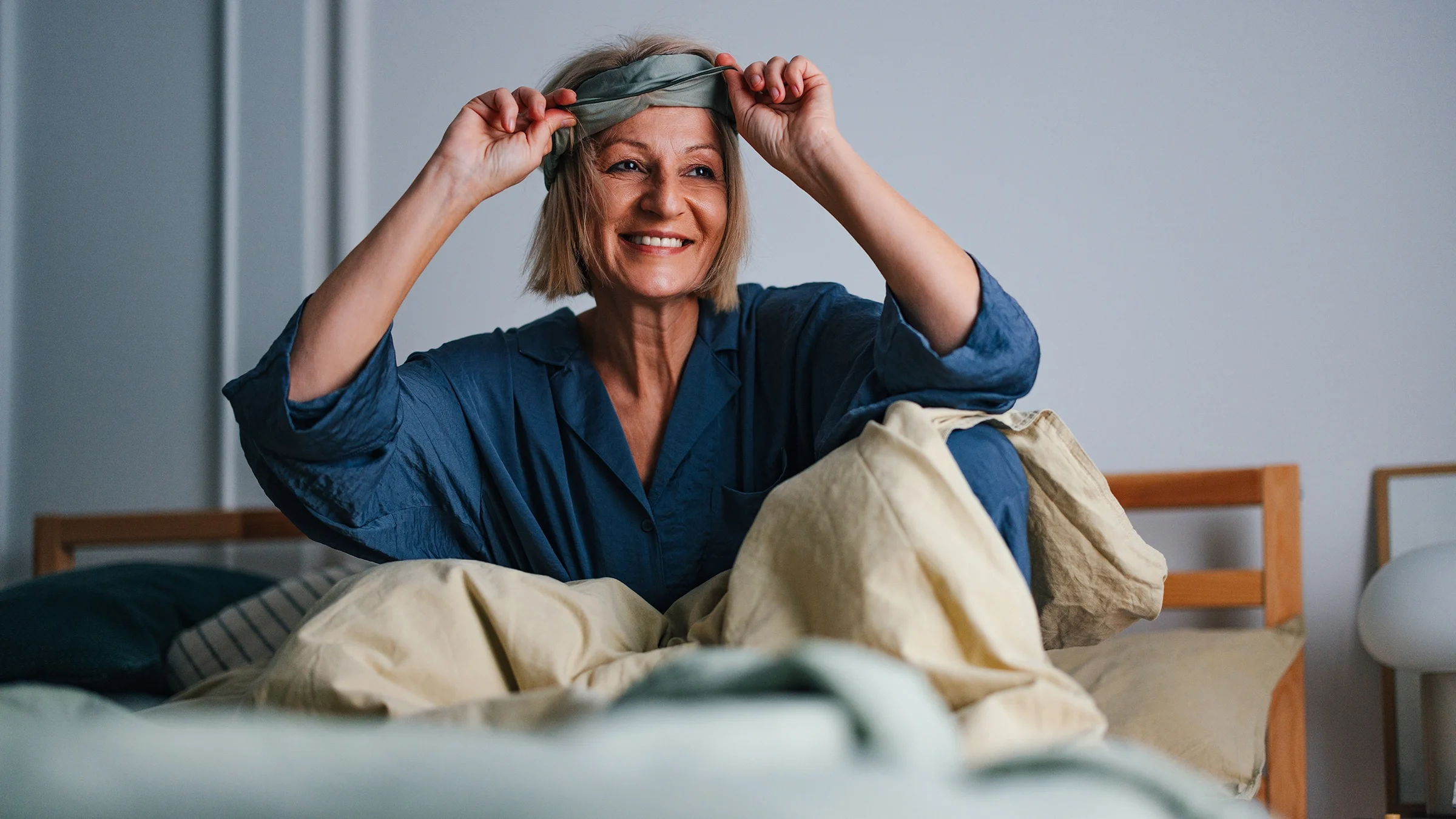 A woman smiles as she takes off her sleeping mask.