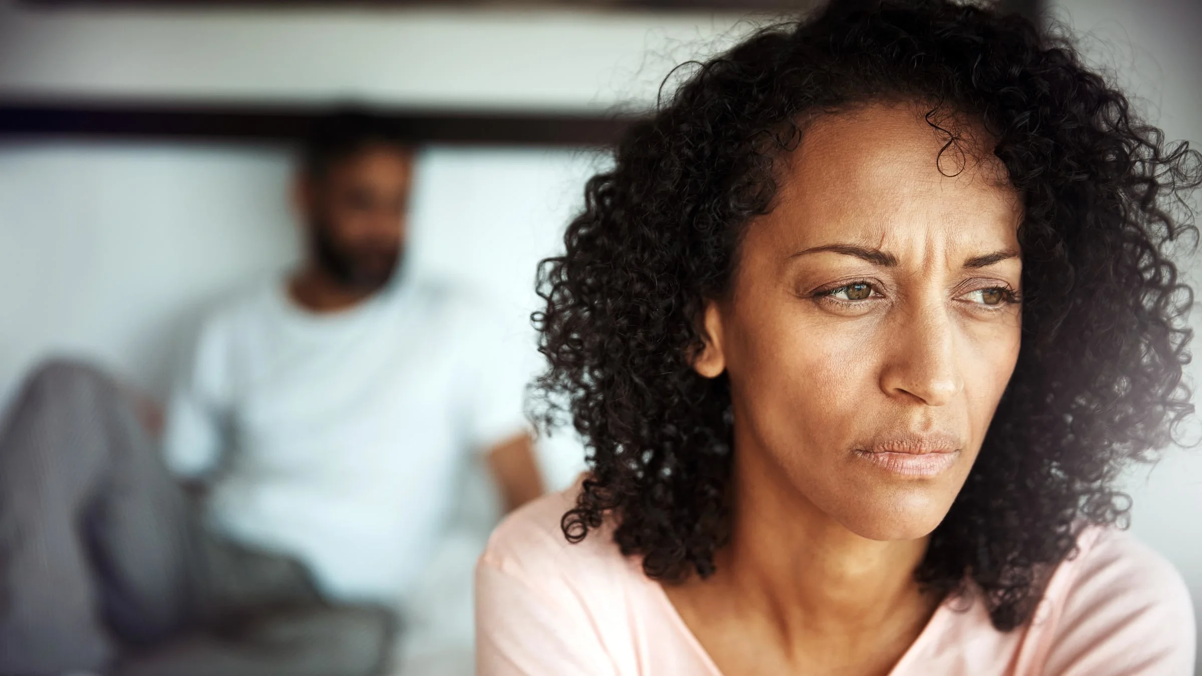 A woman looks upset, while a man is partially visible in the background.