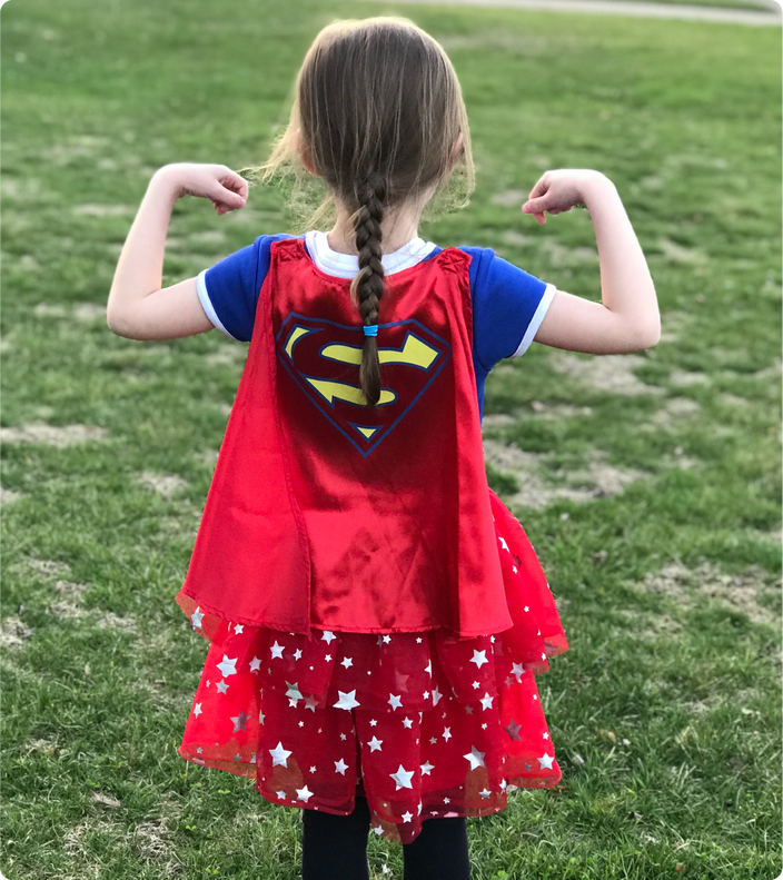 Roger’s daughter in her Superman cape flexing her muscles outside at the park. The view is of her silhouette from the back.