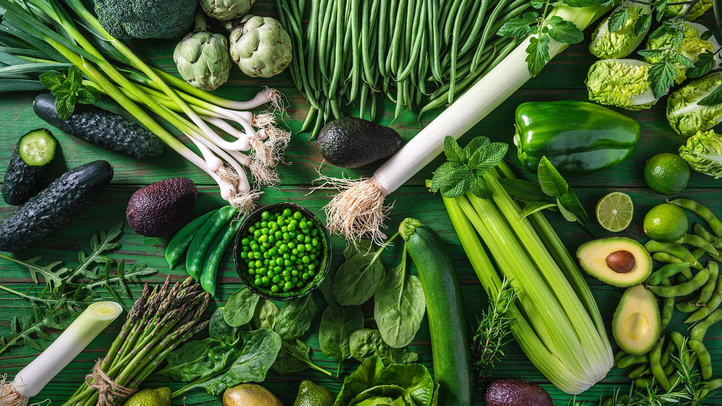 Flat lay of various green vegetables on a green textured background.
MEDITERRANEAN/iStock via Getty Images