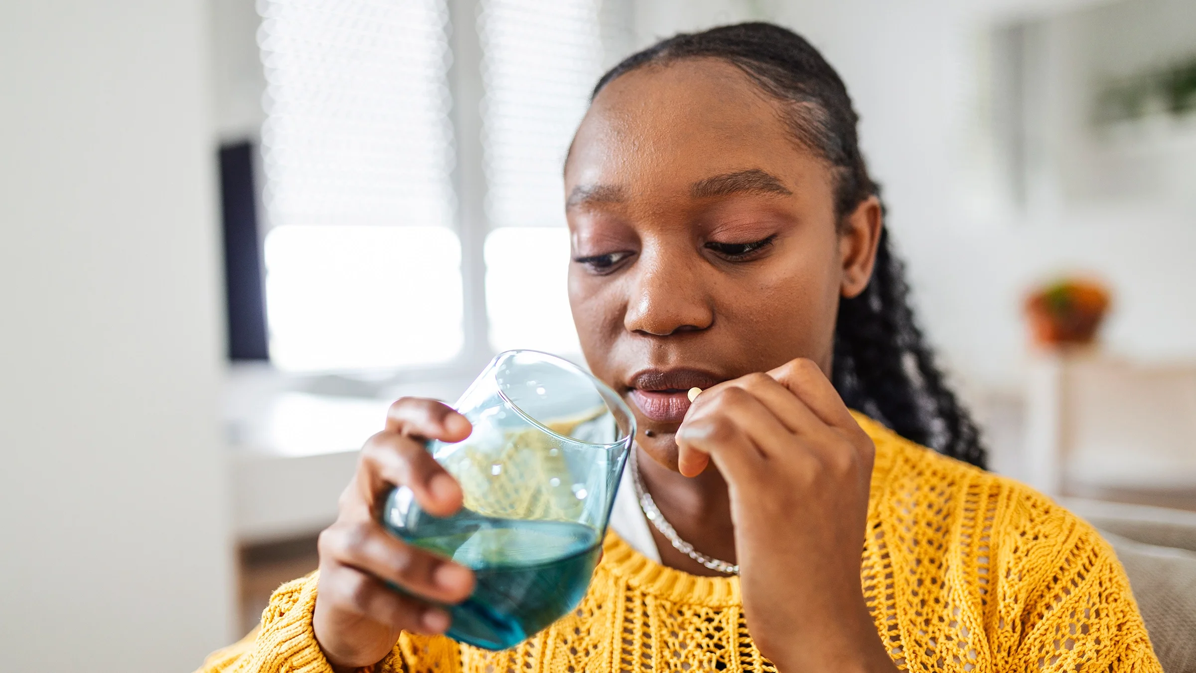 Woman sitting on a sofa and taking a pill.