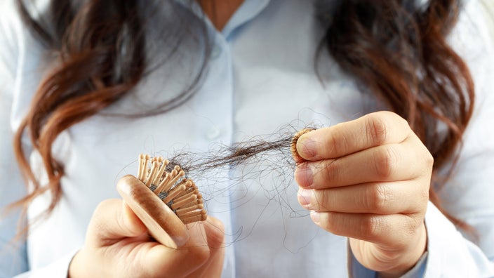 A cropped shot of a woman removing loose hair from her brush.