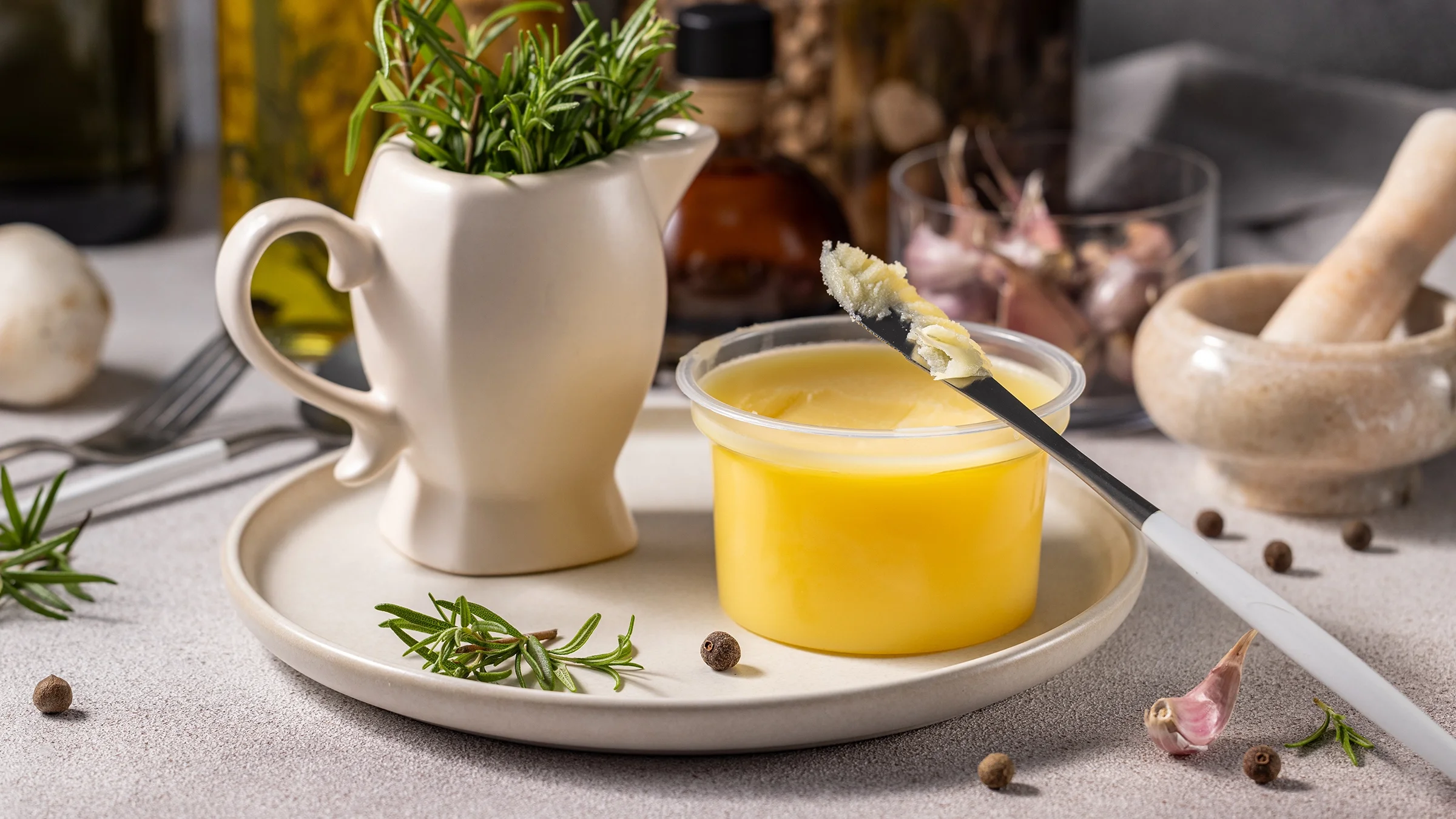 Jar of ghee on a table surface next to herbs.
