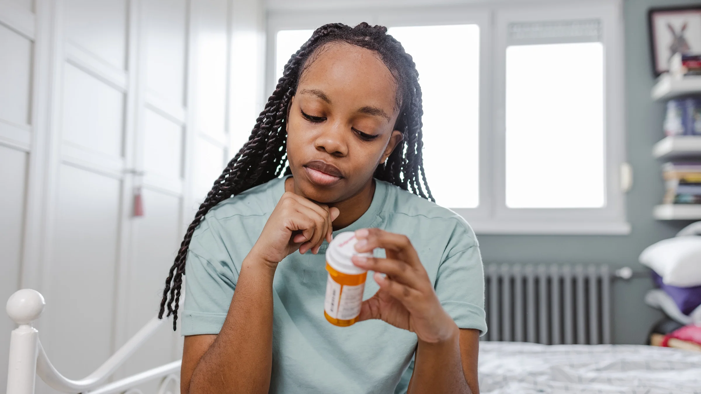 A woman sits on a bed and reads a prescription bottle.
