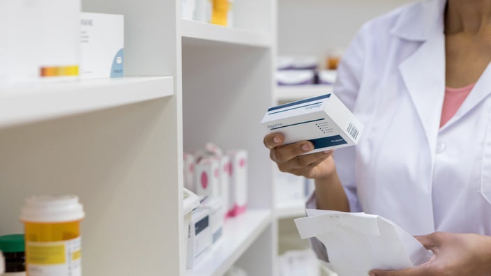 Cropped shot of a pharmacist reviewing a prescription box package next to the prescription wall.