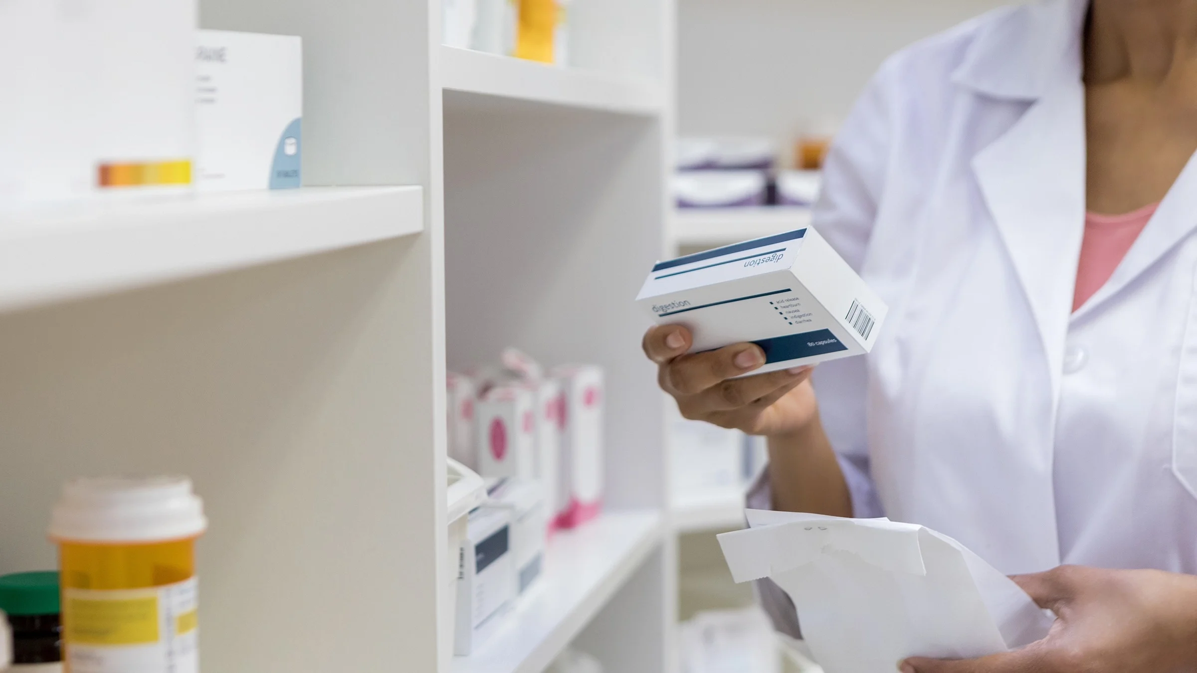 Cropped shot of a pharmacist reviewing a prescription box package next to the prescription wall.