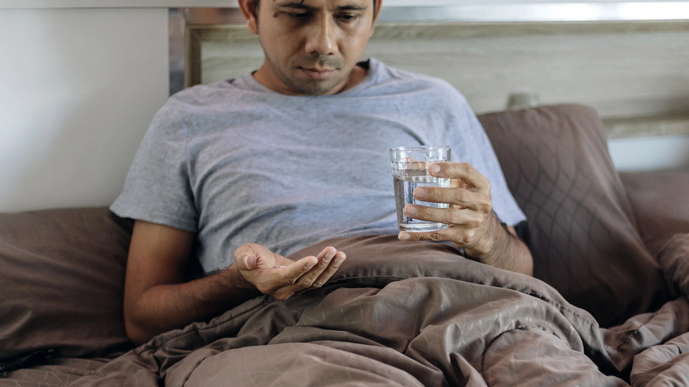 Man taking medication while lying in bed.