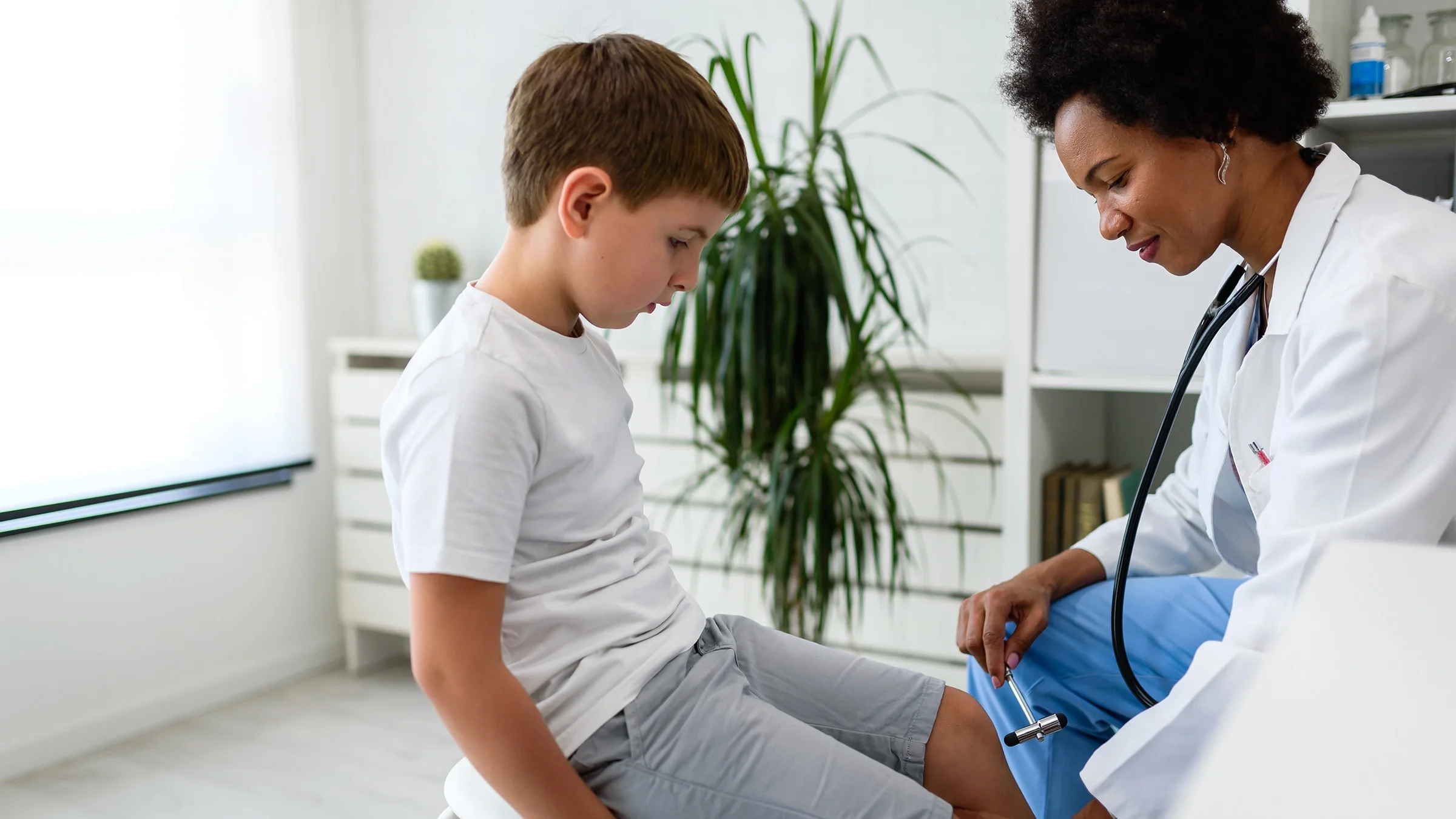Doctor doing a reflex test on a child in the exam room.