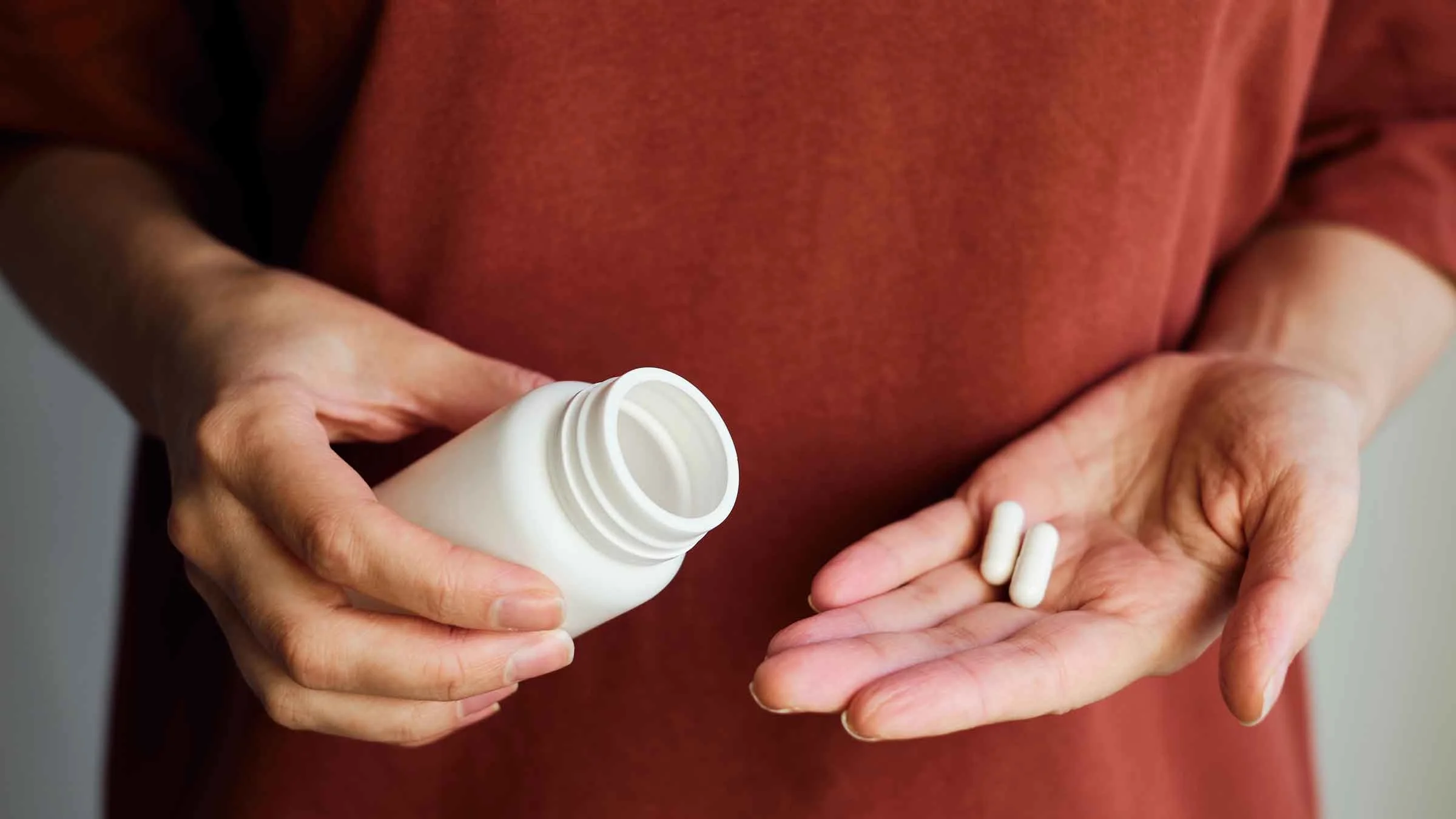 A woman pours pills from a jar onto her hand.