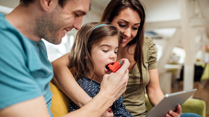 Parents help their daughter use an asthma inhaler.