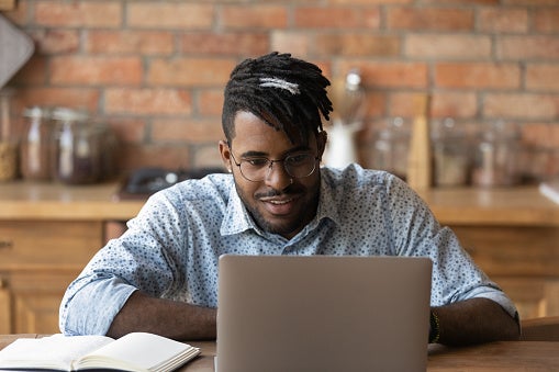 Young man looking up something on his laptop at a coffee shop table.