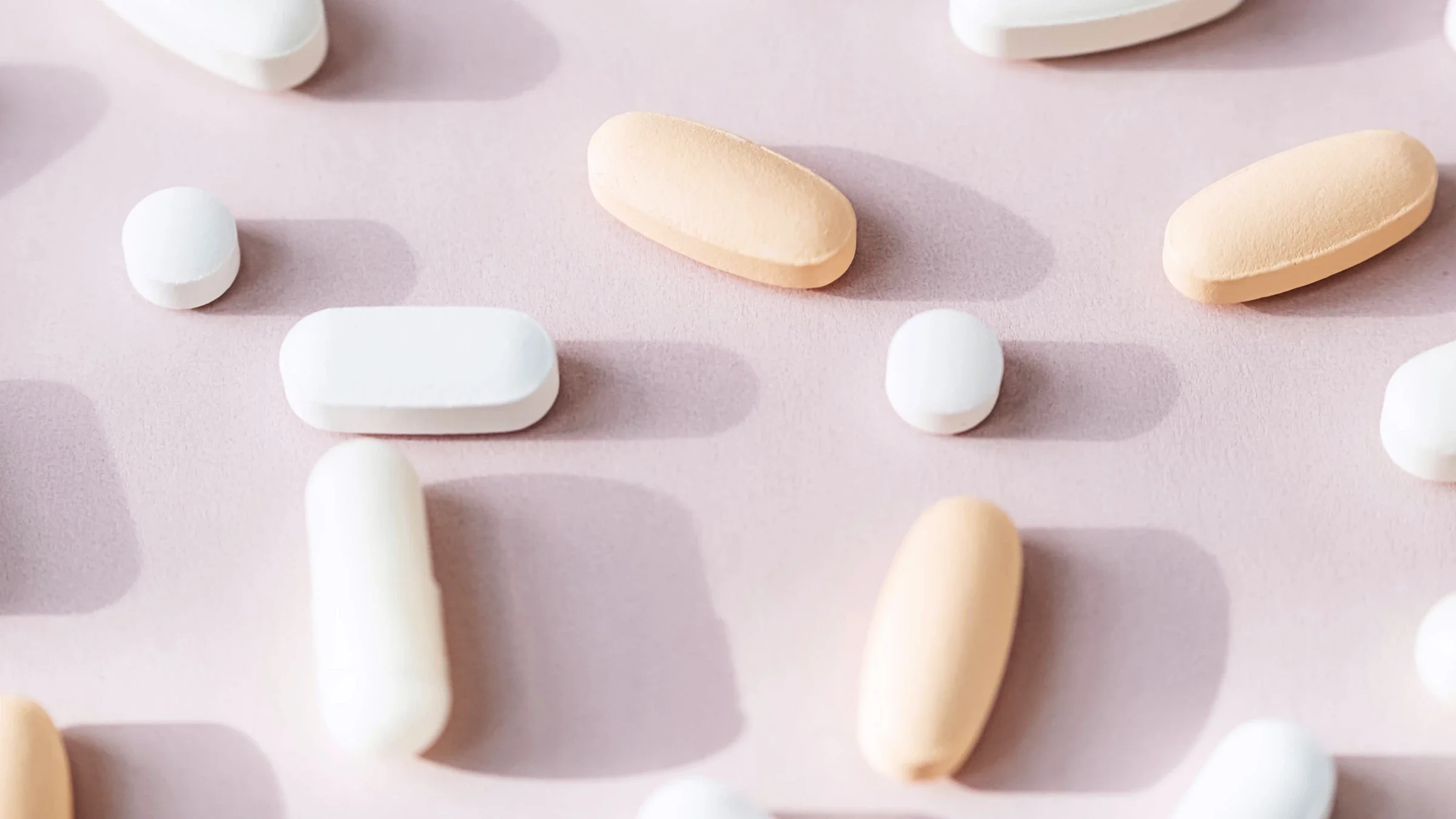 Various white and tan vitamins on a light pink background.